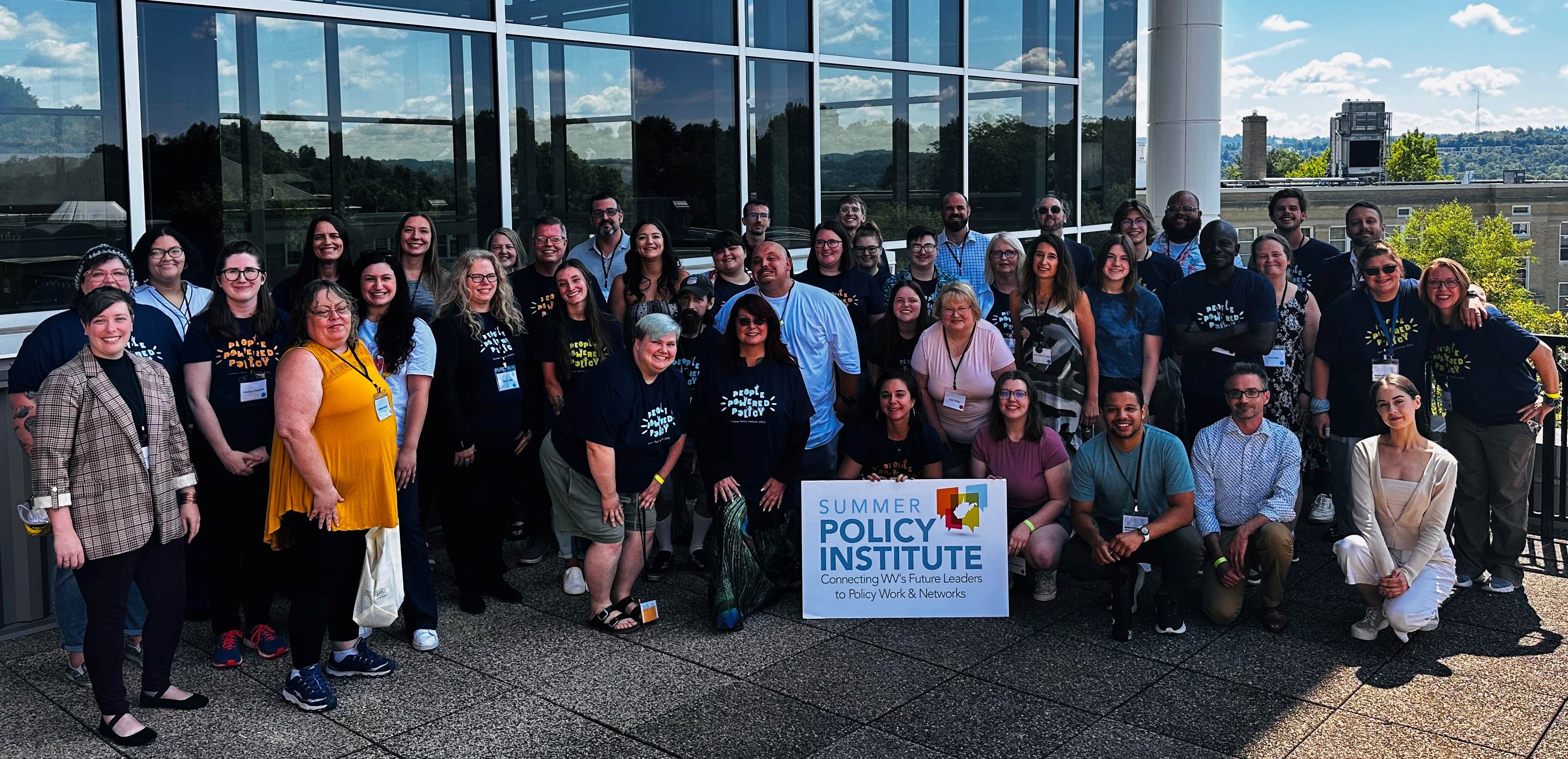 Picture of a large group of people outside with a sign that says 'Summer Policy Institute'